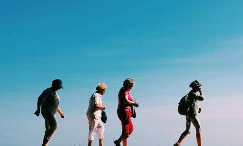 Quatre femmes marchant en file sous un grand ciel bleu, complices, lors d’une promenade